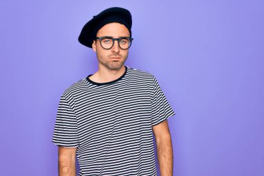 Mor arka plan üzerinde çizgili tişört ve Fransız beresi giyen yakışıklı adam uykulu ve yorgun görünüyor, yorgunluktan yorgun ve akşamdan kalma, sabahları tembel gözler..