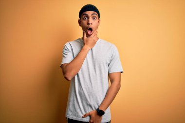 Sarı arka plan üzerine spor giysili yakışıklı Afro-Amerikan sporcusu elleri çenesinde, inanamama, şaşırma ve hayrete düşme ifadesine hayran kaldı.