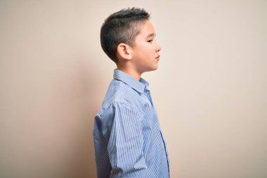 Zarif bir gömlek giyen küçük bir çocuk. İzole edilmiş arka planda duruyor. Yan tarafa bakıyor, rahat poz veriyor, kendine güvenen bir gülümsemesi var..