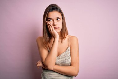 Genç, güzel esmer kız izole edilmiş pembe arka plan üzerinde günlük çizgili tişört giyiyor. Kolları çaprazlanmış depresyondan sıkılmış ve yorgun görünüyor..