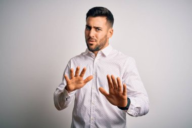 Zarif gömlekli genç adam izole edilmiş beyaz arka planda duruyor. Avuçlarını hareket ettiriyor. Korkmuş ve iğrenç bir ifadeyle reddediyor. Dur ve yasakla.
