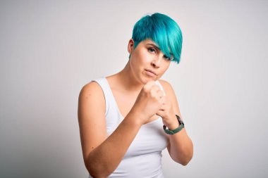 Mavi saçlı, beyaz arka planda rahat tişörtler giyen genç ve güzel bir kadın. Yumruk savunma hareketleriyle kavga etmeye hazır, kızgın ve üzgün bir yüz, sorundan korkuyor.