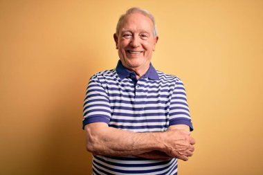 Gri saçlı, donanma çizgili tişört giyen, sarı arka planda duran mutlu yüzlü, kollarını kavuşturup kameraya bakan son sınıf öğrencisi. Pozitif kişi.