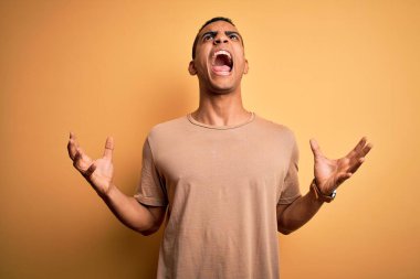 Sarı arka planda sıradan tişörtler giyen genç ve yakışıklı Afro-Amerikalı adam deli gibi bağırıyor ve agresif bir ifade ve kollarla bağırıyor. Hayal kırıklığı konsepti.