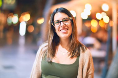 Mutlu ve kendinden emin gülümseyen genç ve güzel bir kadın. Kasaba caddesinde yüzünde gülümsemeyle dikilirken