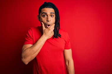 Kırmızı günlük tişörtler giyen Afro-Amerikan Afrikalı genç adam elleri çenesinde, inanamama, şaşırma ve şaşkınlık ifadesi ile büyülenmiş görünüyor.