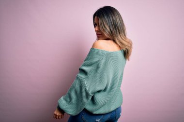 Moda kıyafetleri giyen genç ve güzel bir kadın. Manken, sokak tarzı giyiniyor. Pembe arka planda dikiliyor.