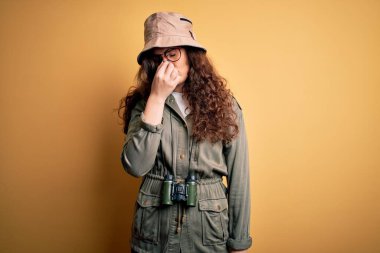 Gezgin şapkası ve dürbünle gezen genç, güzel bir turist kadın. Burnu ve gözleri ovuşturmaktan yorgun düşmüş, yorgun düşmüş ve başı ağrıyormuş. Stres ve hüsran kavramı.