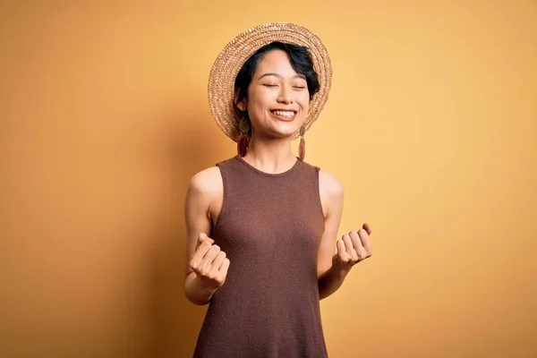 年轻美丽的亚洲女孩穿着休闲装 头戴一顶帽子 头戴黄褐色背景的帽子 高兴而兴奋地举起双臂 做着获胜的手势 微笑着 尖叫着要成功 庆祝概念 — 图库照片