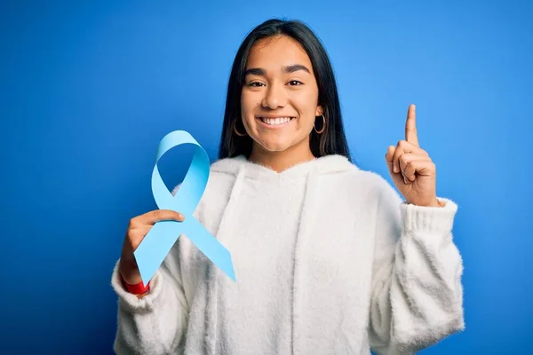 Młoda Azjatka Trzymająca Symbol Niebieskiej Wstążki Nowotworowej Stojącej Nad Odizolowanym — Zdjęcie stockowe