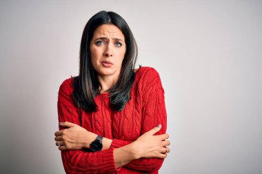 Mavi gözlü genç esmer kadın izole edilmiş beyaz arka planda günlük süveter giyiyor. Kış soğuğu yüzünden titriyor ve donuyor. Yüzünde üzgün ve şok ifadesi var.