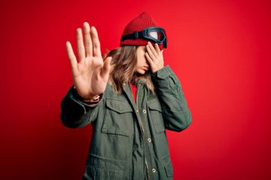 Kayak gözlüğü takan genç sarışın kız ve kayak yaparken kırmızı arka planda gözleri kapayarak hüzünlü ve korku dolu bir ifadeyle jest yapıyor. Utanç verici ve olumsuz bir kavram..