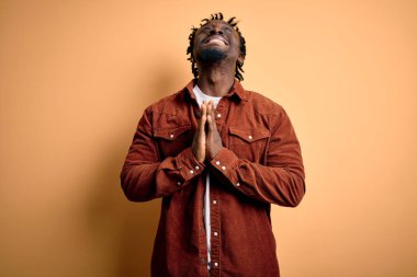 Sarı arka planda sıradan bir ceket giyen genç ve yakışıklı Afro-Amerikalı adam elleri bağlı yalvarıyor ve dua ediyor. Yüzünde umut ifadesi var. Çok duygusal ve endişeli. Yalvarıyorum..