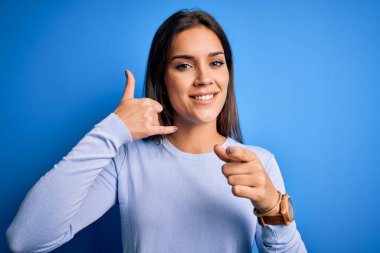 Genç, güzel, esmer bir kadın mavi arka plan üzerinde dikilip gülümseyen telefonda konuşan ve seni işaret eden bir süveter giyiyor. Ara beni..