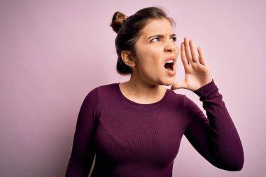 Güzel, genç bir kadın pembe izole edilmiş arka planda gelişigüzel çörek saçı takmış el ele tutuşarak bağırıyor ve çığlık atıyordu. İletişim konsepti.