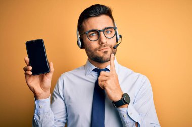 Çağrı merkezinden gelen müşteri hizmetleri kulaklığı olan bir işletmeci akıllı telefon ekranı ciddi bir yüz ifadesi gösteriyor. Soru hakkında düşünüyor, kafası karışık bir fikir.