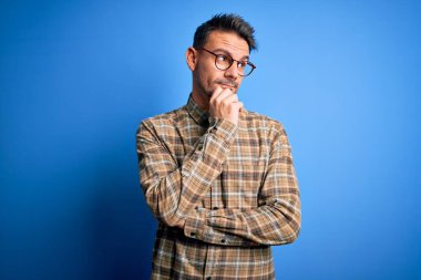 Mavi arka planda, elleri çenesinde, sıradan gömlek ve gözlük takan genç yakışıklı bir adam soru sorarken, düşünceli bir ifade takınıyor. Düşünceli bir yüzle gülümsüyor. Şüphe kavramı.