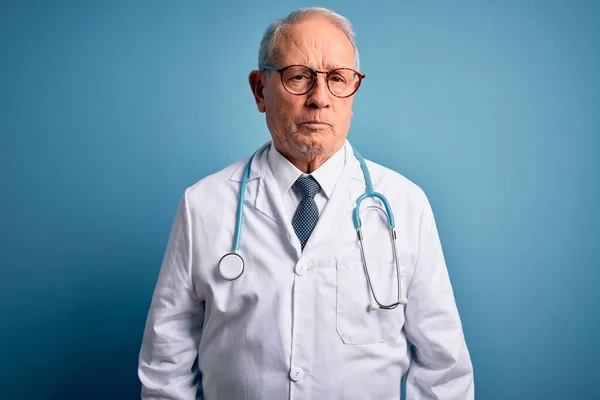 Starszy Siwy Lekarz Noszący Stetoskop Płaszcz Medyczny Niebieskim Tle Sceptyczny — Zdjęcie stockowe