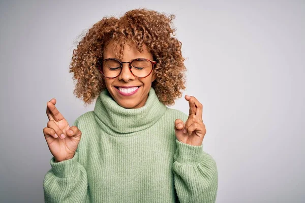 タートルネックのセーターを着た若い美しいアフリカ系アメリカ人女性と眼鏡ジェスチャーの指は希望と目を閉じて笑顔を越えました 幸運と迷信の概念 — ストック写真