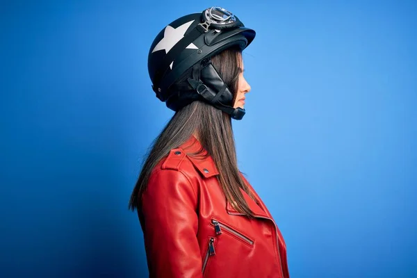 Young beautiful brunette motorcycliste woman wearing motorcycle helmet and jacket looking to side, relax profile pose with natural face with confident smile.
