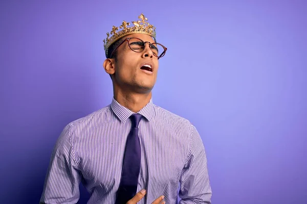 若いハンサムなアフリカ系アメリカ人の男性の胃の上に手で紫色の背景に王の黄金の冠を身に着けているので 吐き気 痛みを伴う病気が具合が悪い アチェの概念 — ストック写真