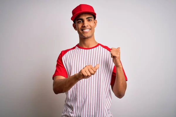 若いハンサムなアフリカ系アメリカ人のスポーツマンは ストライプの野球Tシャツとキャップを身に着けています手と親指で後ろを指して 自信を持って笑って — ストック写真