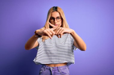 Genç, sarışın, çizgili tişört ve gözlük takan, mor arka planda reddedilmiş güzel bir kadın.