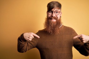 Sakallı, sarı arka planda kışın süveter giyen yakışıklı kızıl saçlı, kendine güvenen, kendini gururlu ve mutlu gösteren bir adam..