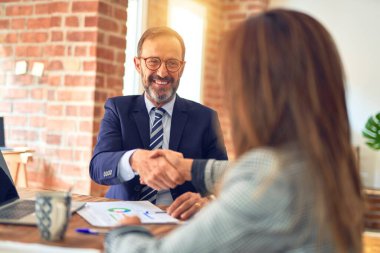 Mutlu ve kendinden emin gülümseyen iki orta yaşlı iş adamı. Birlikte çalışırken gülümseyerek ofiste el sıkışırken.