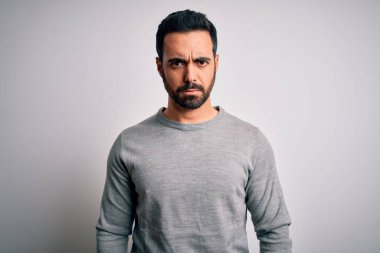 Sakallı, sıradan süveter giyen, beyaz arka planda duran, kuşkucu ve gergin, sorun yüzünden üzgün, yakışıklı genç bir adam. Negatif kişi.