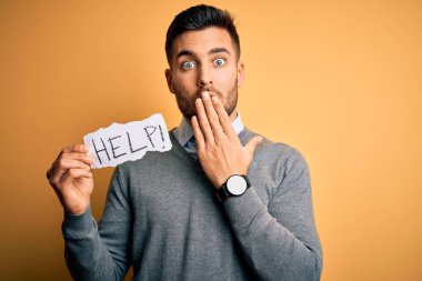 Çok çalışan genç iş adamı, sarı arka plan kapağı üzerinde kağıt tutarak yardım istiyor. Ağzı kapalı, utançla dolu, korkunun ifadesi, sessizlikten korkmak, gizli bir konsept.