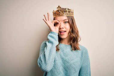Soyutlanmış arka planda kraliçe tacı takan genç sarışın kız el hareketleriyle gülümsüyor ve mutlu yüzle parmaklarının arasından bakıyor..