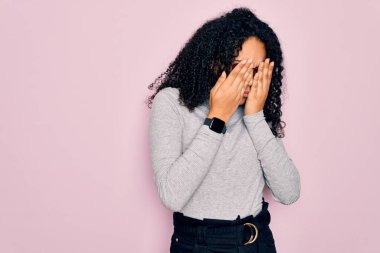 Genç Afro-Amerikalı kadın balıkçı yaka kazak ve pembe arka plan üzerine gözlük takıyor yorgunluk ve baş ağrısı için gözlerini ovuşturuyor, uykulu ve yorgun bir ifade takınıyor. Görüş sorunu