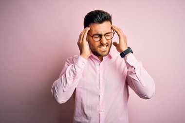 Zarif bir gömlek ve gözlük takan yakışıklı bir adam pembe arka planda dikiliyor. Baş ağrısı yüzünden çaresiz ve stresli. Çünkü acı ve migren. Ellerini başının üstüne koy..