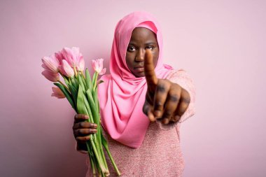 Genç Afro-Amerikan artı cüsseli kadın elinde pembe lale buketi tutuyordu. Parmağını kaldırmış ve kızgın bir ifade sergiliyordu.