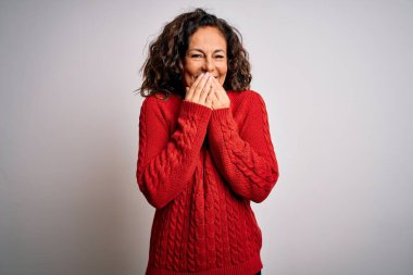Orta yaşlı esmer kadın, günlük süveter giyip izole edilmiş beyaz arka planda dikiliyor gülüyor ve utanıyor kıkırdıyor ağızlarını ellerle, dedikodularla ve skandallarla kapatıyor.