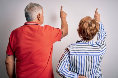 Üst düzey güzel çift, izole edilmiş beyaz arka planda yan yana duruyorlar. Geriye doğru poz veriyorlar. Parmaklarını öne doğru uzatarak.