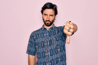 Pembe arka planda hippi tarzı giyinmiş genç, yakışıklı, bohem bir adam. Mutsuz ve sinirli görünüyor. Reddedilmiş ve olumsuz. Kötü ifade.