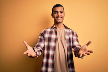 Genç, yakışıklı, Afro-Amerikalı bir adam sarı arka planda dikilmiş neşeli gülümseyerek yardım eli uzatıyor ve kabul ediyor..