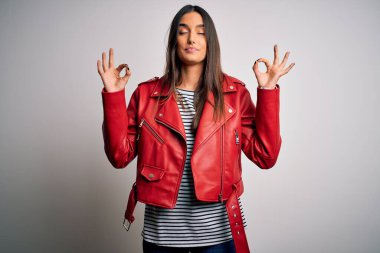 Genç ve güzel esmer kadın, günlük çizgili tişört ve kırmızı ceket giyip rahatlıyor ve gözleri kapalı gülümsüyor parmaklarıyla meditasyon hareketi yapıyor. Yoga konsepti.