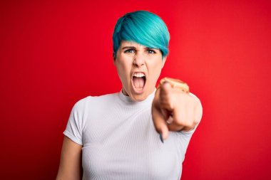 Kırmızı arka plan üzerine sıradan tişörtler giyen mavi saçlı genç ve güzel bir kadın kameraya kızgın ve sinirli olduğunu gösteriyor.