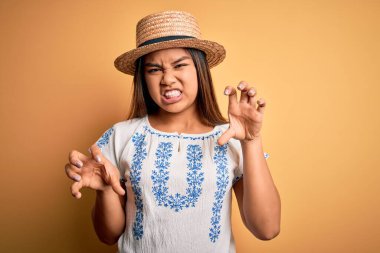 Sarı arka planda dikilen günlük tişört ve şapka giyen genç, güzel Asyalı kız kedi gibi gülüyor, agresif ve seksi bir ifade takınıyor.