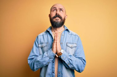 Sakallı, sıradan bir kot ceket ve çizgili tişört giyen yakışıklı kel adam elleri bağlı yalvarıyor ve dua ediyor. Yüzünde umut ifadesi var. Çok duygusal ve endişeli. Yalvarıyorum..