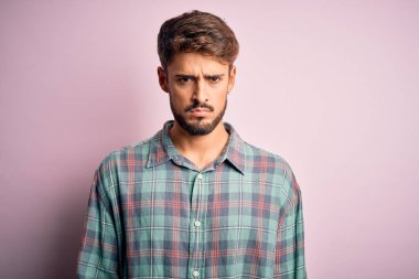 Sakallı, sıradan bir gömlek giyen, pembe arka planda duran, kuşkucu ve gergin, sorun yüzünden somurtan genç, yakışıklı bir adam. Negatif kişi.