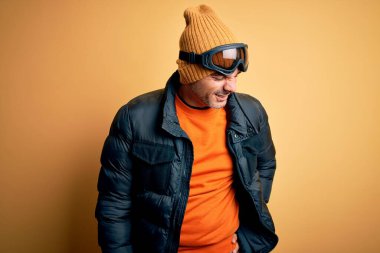 Genç kayakçı, kar sporu kıyafetleri içinde kayak yapıyor kayak gözlüğü takıyor sırt ağrısı çekiyor, elle dokunuyor, kas ağrısı çekiyor.