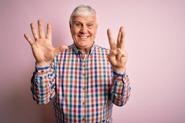 Kıdemli yakışıklı, beyaz gömlekli, pembe arka planda yalnız ve mutlu ve kendinden emin bir şekilde gülümseyerek sekiz numarayı işaret ediyor..