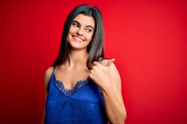 Genç ve güzel esmer kadın zarif ve rahat iç çamaşırı giyiyor mutlu yüzüyle gülümsüyor ve başparmağıyla yüzünü gösteriyor..