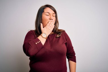 Güzel esmer ve cüsseli bir kadın izole edilmiş beyaz arka plan üzerine gündelik bir kazak giyiyor. Elle ağzını kapatmaktan sıkılmış. Huzursuz ve uykulu..