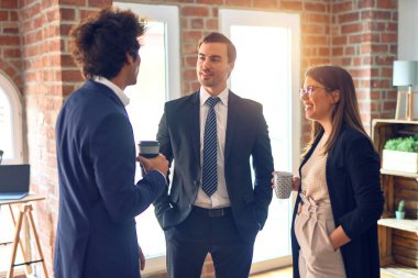 Mutlu ve kendinden emin bir şekilde gülümseyen genç ve güzel iş adamları kahve içip ofiste konuşuyorlar.