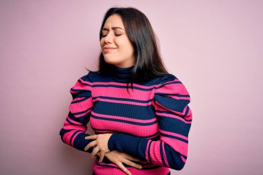 Genç esmer, zarif bir kadın pembe izole edilmiş arka plan üzerine çizgili tişört giyiyor. Midesinde hazımsızlık, acı verici bir hastalık var. Ache kavramı.